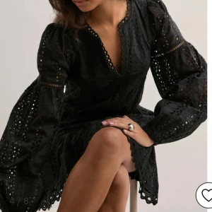 Svart kort klänning från Nelly - Supersnygg svart kort klänning från Nelly med broderade detaljer och v-ringning. Klänningen har långa puffärmar, markerad midja och volangkant nertill. Perfekt för dig som gillar romantisk och trendig stil med extra detaljer.