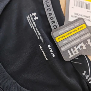 Svart träningst-shirt från Under Armour - Svart kortärmad t-shirt från Under Armour med diskret logga på bröstet och ärmen. Tillverkad i lätt och stretchig polyester, perfekt för träning. Snygg, sportig passform och UA HeatGear-material som andas och håller dig sval.helt oanvänd möts upp i goteborg!