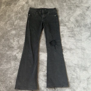 Svarta bootcut jeans med hål - Säljer ett par svarta bootcut jeans med snyggt sliten look och stort hål på ena benet. Klassisk femficksmodell med dragkedja och knapp. Jeansen har en mörk tvätt och är tillverkade i mjukt denimtyg. Som ni ser är lappen borta så jag vet inte storlek eller butik, men jag är 168 cm lång och de passar mig bra i längden💓