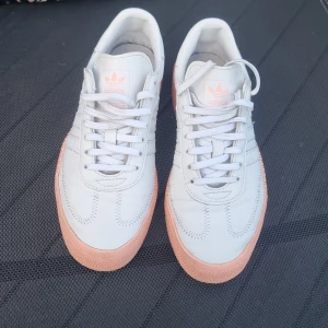 Adidas Samba Rose vit/rosa/aprikos sneakers - Adidas Samba Rose sneakers i vitt skinn med ljusrosa/aprikos platåsula. Klassisk design med tre ränder på sidan, snörning och rund tå. Adidas-logga och detaljer i rosa/aprikos på plös och sula. Storlek 36 2/3. ( Passar mig som har 36-36.5).