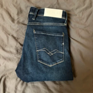 Replay mörkblå jeans herr 32/32 (prisförslag) - Snygga mörkblå jeans från Replay med klassisk femficksdesign och kontrastsömmar. Jeansen har raka ben och tydlig Replay-logga på bakfickan samt patch i vitt vid linningen. Perfekta för dig som gillar stilrena och tidlösa jeans.