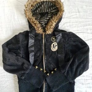 Y2K-hoodie med pälsluva - Säljer denna fantastiska Y2K-hoodie från Wójsic Vogue Generation 🎀 Svart, croppad modell med pälsluva och markerad midja.  Guld och svartrandigt foder, sidenband. Guldiga knappar vid ärmsluten. Storlek 140 på lappen men väkdigt stor i storleken, passar som en vuxen XS. Normala bruksspår men inga anmärkningsvärda defekter!  Pris är självklart förhandlingsbart 😊 Hör gärna av er vid frågor och glöm inte att kolla in garderoben för fler liknande plagg! 💕