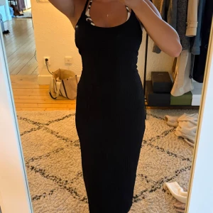 Svart långklänning med slits - Säljer en svart långklänning med smala axelband och snygg slits baktill. Klänningen har en strukturerad, lite krinklad yta och sitter figurnära. Perfekt för dig som gillar en stilren och enkel look med en twist.