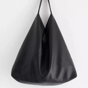 Stor svart axelväska/hoboväska - Säljer en stor och stilren svart axelväska i skinnimitation. Väskan har minimalistisk design med triangulär form och kort axelrem, perfekt för dig som gillar en clean och modern look. Rymmer allt du behöver till skolan eller stan. Nypris: 399kr