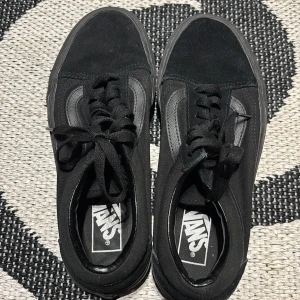 Svarta Vans Old Skool sneakers - Klassiska svarta Vans Old Skool sneakers med svart sidestripe och snörning. Ovandel i canvas och mocka, samt den ikoniska gummisulan i brunt. Perfekta för en streetstyle-look och funkar året runt.