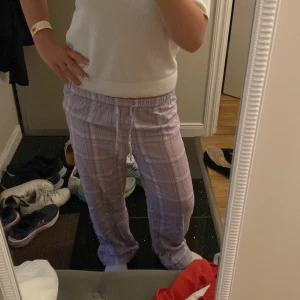 Lila rutiga byxor från Gina Tricot - Säljer ett par lila rutiga byxor från Gina Tricot med dragsko i midjan. Byxorna har avslappnad passform och är perfekta för chill dagar hemma. Mjukt material och elastisk midja för extra komfort.