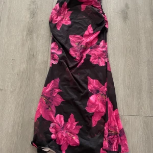 Svart lång kjol med rosa blommor - Supersnygg lång kjol med svart bas och stora, iögonfallande rosa blommor. Kjolen har en figurnära passform och är tillverkad i ett mjukt, stretchigt material. Perfekt för dig som vill sticka ut med ett färgstarkt mönster.