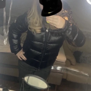 Svart Moncler Maya storlek 2 - Helt ny Moncler jacka som används fåtal gånger, jag säljer för att jag inte behöver den. Snygg svart pufferjacka från Moncler med glansig finish och huva. Jackan har dragkedja framtill, Moncler-logga på ärmen och quiltad design. Perfekt för kalla dagar när du vill hålla stilen och värmen. Vid snabb affär kan man få jackan för ett billigare pris😊😊