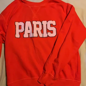 Röd sweatshirt med PARIS-tryck H&M XS - Cool röd sweatshirt från H&M i storlek XS med stort vitt PARIS-tryck på bröstet. Tröjan har rund halsringning och långa ärmar, perfekt för dig som vill sticka ut med en färgstark och trendig look.