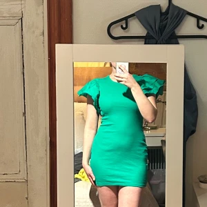 Grön ribbad kortklänning från Zara - Supersnygg grön kortklänning från Zara med ribbad struktur och volangiga axlar. Tight passform som framhäver figuren och coola detaljer på ärmarna. Perfekt för dig som vill sticka ut med färg och form! Den har en varmare ton i verkligheten, använd fåtal gånger💚