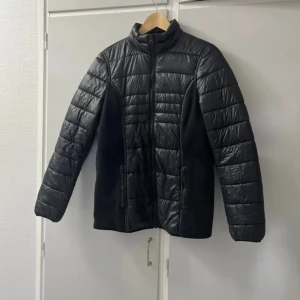 Svart pufferjacka gravid från Bonprix, stl 36 - Svart pufferjacka för gravida /mammajacka från Bonprix Collection i storlek 36. Jackan har quiltade partier i glansigt syntetmaterial och mjuka sidor i tyg, hel dragkedja framtill och två fickor med dragkedja. Insidan är fodrad i orange. Perfekt för kyliga dagar.