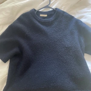 Mörkblå stickad tröja från Gina  - Mysig mörkblå stickad tröja från gina med korta ärmar och rund hals. Perfekt för lager-på-lager och ger en chill vibe till din outfit. Passar dig som gillar enkel men stilren look.