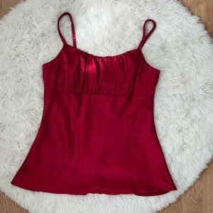 Röd linnetopp från A. Byer - Snygg röd linnetopp från A. Byer med glansigt tyg och flätade axelband. Passar bäst storlek 38, men även storlek 36 om du har större byst (>88cm)