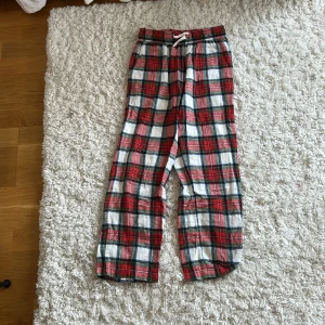 Röd-rutiga mjukisbyxor från Lindex - Mysiga mjukisbyxor från Lindex i röd, vit och blå rutig design. Byxorna har resår i midjan med snörning och är gjorda i mjuk bomull. Perfekta för chill dagar hemma eller som pyjamasbyxor.