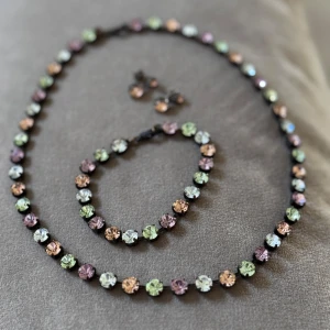 Pastellfärgat smyckeset strass - Snyggt smyckeset med halsband, armband och örhängen. Alla delar har runda, gnistrande stenar i pastellfärger som rosa, grön, lila och ljusblå. Stenarna sitter i mörka fattningar och ger en glittrig och färgglad look. Perfekt för dig som gillar att sticka ut. 