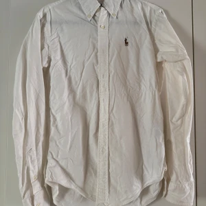 Vit skjorta från Ralph Lauren - Vit skjorta från Ralph Lauren med broderad logga på bröstet. Skjortan har lång ärm, knappar framtill och button down-krage.🤍