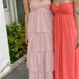 Ljusrosa långklänning med volanger - Superfin ljusrosa långklänning med flera lager volanger och bandeau-topp. Klänningen är axelbandslös och har en flowy, romantisk look. Perfekt för sommarens alla tillfällen när du vill känna dig extra söt och drömmig. Använd en gång! 💕Köpt för 699kr från Nelly 