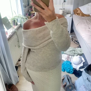 Beige offshoulder stickad tröja - Supermysig beige stickad tröja med offshoulder-design och långa ärmar. Tröjan har en bred, vikt krage som ger en chill och trendig vibe. Perfekt att styla med kjol eller jeans för en snygg look.