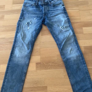 Slim fit jeans från Jack & Jones - Snygga blå slim fit jeans från Jack & Jones, modell Glenn. Jeansen har slitna detaljer och hål på låren för en cool, avslappnad look. Klassisk femficksmodell i mjukt bomullsjeans med dragkedjegylf.