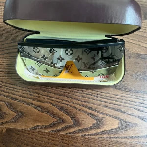 Lv monogram solglasögon - Snygga solglasögon med svart båge och stora, rektangulära linser i grått med klassiskt monogrammönster. Glasögonen har en futuristisk vibe och levereras med originaletui, putsduk och box. Perfekt accessoar för dig som vill sticka ut.