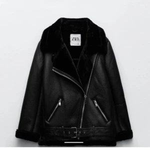 Svart skinnjacka från Zara med bälte - Snygg svart skinnjacka från Zara med bred krage i fuskpäls, sned dragkedja och bälte i midjan. Jackan har två dragkedjefickor och detaljer i silver. Perfekt för dig som vill ha en edgy look.