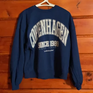 Blå sweatshirt från Bershka XS - Mörkblå sweatshirt från Bershka i storlek XS med stort tryck 'Copenhagen Since 1989' framtill. Tröjan har rund hals, långa ärmar och en klassisk loose passform. Perfekt för dig som gillar streetstyle och collegevibe.