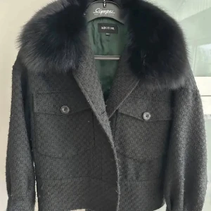 Svart jacka med päls från Meotine - Snygg svart jacka från Meotine med stor svart pälsig krage. Jackan har två bröstfickor med knappar och en croppad passform. Materialet är strukturerat och ger en lyxig känsla. Perfekt för dig som vill sticka ut med stil.