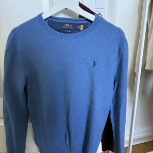 Blå tröja från Polo Ralph Lauren - Snygg blå tröja från Polo Ralph Lauren i mjuk pima bomull. Klassisk rund halsringning, diskret broderad logga på bröstet och långärmad modell. Perfekt för dig som gillar stilrena och tidlösa plagg med premiumkänsla.