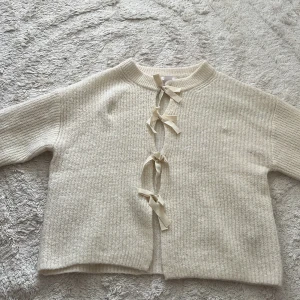 Beige stickad kofta med knyt från Gina Tricot - Superfin beige stickad kofta från Gina Tricot med tre dekorativa knytband framtill. Koftan har långärmad modell, ribbade muddar och en mysig, lite loose passform. Perfekt för lager på lager och chill dagar.