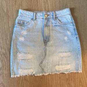 Ljusblå jeanskjol från FB Sister storlek XS - Snygg ljusblå jeanskjol från FB Sister i storlek XS. Kjolen har slitna detaljer, fransad nederkant och klassiska fickor både fram och bak. Perfekt för dig som gillar en avslappnad och trendig stil.