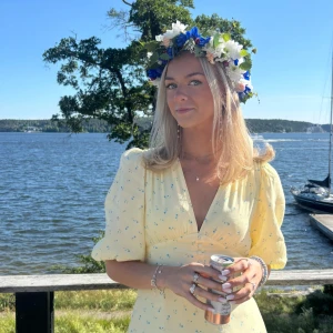 Adoore klänning - Superfin ljusgul kortklänning med små blå blommor, v-ringning och puffiga korta ärmar. Klänningen har markerad midja och lätt utsvängd kjol, perfekt för sommarens alla tillfällen. Söt och feminin stil med romantiska detaljer.