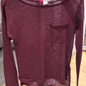 Vinröd tröja  - Vinröd, tunn stickad tröja från Gina Tricot. Modellen har rund halsringning, lång ärm och en liten bröstficka. Materialet är mjukt och lätt,  gör den skön att bära.