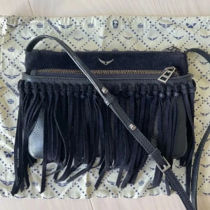 Zadig väska - Väska från Zadig & Voltaire med fransar. Crossbody väska. Väskan är marinblå men ser lite svart ut på bilderna. Väska har några fläckar på fransarna (se sista bilden) och någon fläck på insidan av väskan, men inget som syns särkilt mycket när man har på sig väskan.