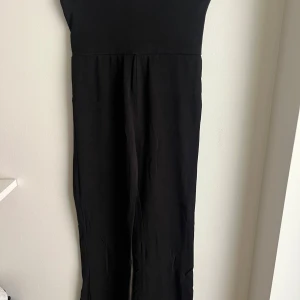 Svart byxdress i mjukt material - En svart byxdress i mjukt och stretchigt tyg. Modellen har långa ben och är ärmlös, perfekt för en clean och enkel look. Passar dig som gillar bekväma plagg med stilren vibe. Byxorna är från gekås💞