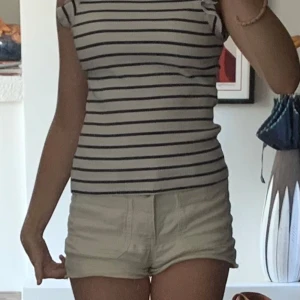 Randig ribbad topp med volangärm - Supersöt topp i vitt med marinblå ränder och volangdetaljer på axlarna. Ribbad struktur som ger en snygg passform och ärmlös design. Perfekt för en chill sommardag eller när du vill ha en fräsch look.