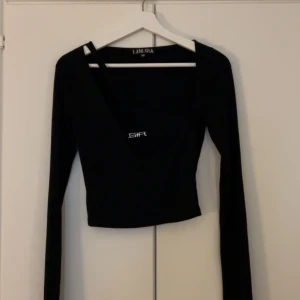Svart croppad topp från I.AM.GIA - Säljer en svart croppad topp från I.AM.GIA med lång ärm och fyrkantig ringning. Toppen har en liten vit logga framtill och är i stretchigt material. Perfekt för en trendig look.