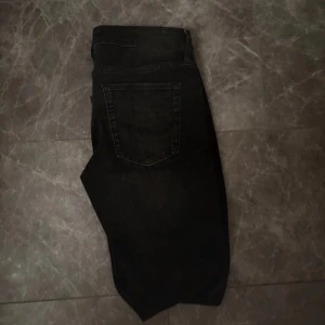 Svarta slim jeans från Jack & Jones - Säljer ett par svarta slim fit jeans från Jack & Jones, modell Glenn. Jeansen har klassisk femficksdesign, knappgylf och smal passform. Perfekta för dig som gillar en stilren och enkel look.