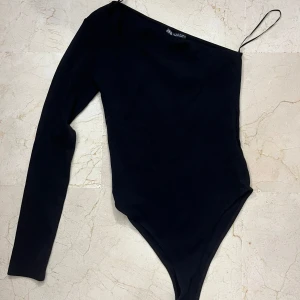 Svart oneshoulder body från Zara - Säljer en svart body från Zara med oneshoulder-design och lång ärm på ena sidan. Så fin vid lite finare tillfällen. Enbart använd en gång💞