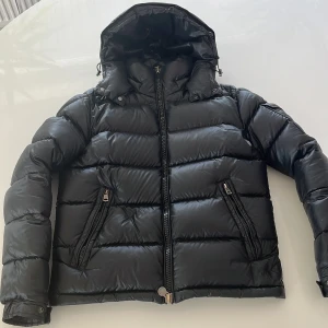 Svart monclear maya jacka  - Säljer en svart dunjacka från Moncler med huva och dragkedja framtill. Jackan har två fickor med dragkedja och Moncler-logga på ärmen. Perfekt för kyliga dagar och riktigt snygg passform.