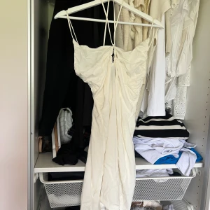 Krämfärgad omlottklänning med smala axelband från HM - Säljer en vit långklänning från HM med smala axelband och omlottdetalj framtill. Klänningen har en lätt rynkad effekt och är tillverkad i ett tunt, mjukt material som passar perfekt till sommaren.