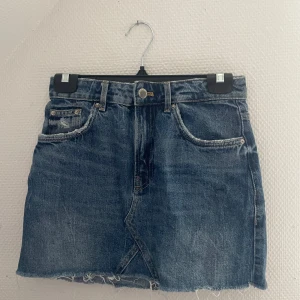 Blå jeanskjol från authentic denim  - Säljer en klassisk blå jeanskjol från authentic denim med rå kant nertill och slitna detaljer. Kjolen har fem fickor och knappstängning framtill. Perfekt för en avslappnad och trendig look.