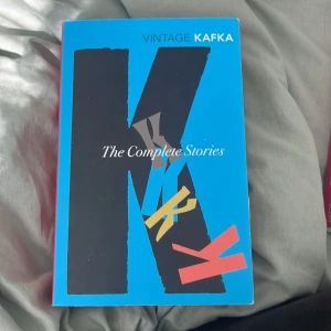 The Complete Stories: Kafka - Säljer boken 'The Complete Stories' av Kafka, utgiven av Vintage. Omslaget är blått med en stor svart bokstav K och färgglada detaljer. Perfekt för dig som vill läsa alla Kafkas noveller samlade i en volym.