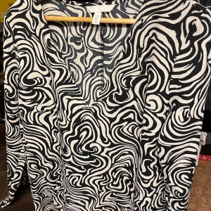 Svartvit mönstrad blus från H&M - Säljer en stilren svartvit blus från H&M med ett unikt abstrakt mönster. Blusen har långa ärmar och en rund halsringning. Perfekt för att ge din outfit en modern touch. 🖤🤍
