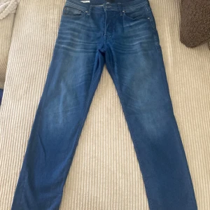 Blå jeansbyxor från Jack & Jones - Säljer ett par klassiska blå jeans från Jack & Jones med fem fickor och normal passform. Byxorna har en snygg tvätt och subtila slitningar för en avslappnad look. Perfekta till vardags och passar till det mesta.