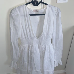 Skolavslutningsklänning från Nelly - Säljer en vit klänning från Nelly i storlek 36. Klänningen har lång ärm, djup v-ringning och markerad midja med smock. Perfekt för sommarens tillfällen och har en luftig känsla.