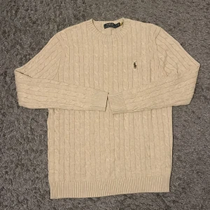 Ljus beige tröja från Ralph Lauren - STORLEK M. Klassisk beige kabelstickad tröja från Polo Ralph Lauren. Långa ärmar och broderad pony på bröstet. Perfekt för stilrena outfits. Nästan helt oanvänd och helt ren. PRISET KAN DISKUTERAS