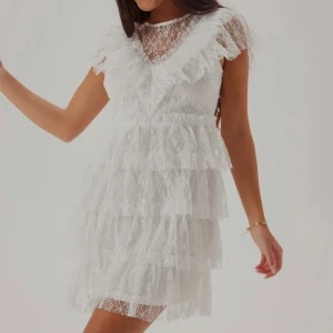 Studentklänning  - Superfin vit kortklänning i spets med flera lager volanger och rund halsringning. Prislapp kvar.
