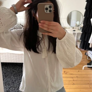 Vit blus med broderade detaljer och knytband - Säljer en fin vit blus från l.o.g.g x H&M med broderade detaljer på ärmarna och knytband vid halsen. Perfekt för vår och sommar!