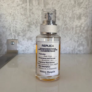 Maison Margiela Jazz Club Eau de Toilette - Maison Margiela Jazz Club är en parfym med varm, bärnstensfärgad vätska i en genomskinlig glasflaska med silverfärgad spraykork. Doften har inslag av söt tobak, vanilj och rom, inspirerad av jazzklubbens atmosfär.
