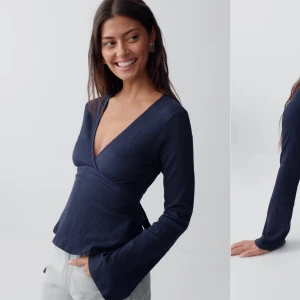 Mörkblå omlottopp med knytband - Snygg mörkblå omlottopp med v-ringning och långa ärmar. Toppen har ett knytband i midjan som ger en fin passform och är tillverkad i ett lätt strukturerat material.